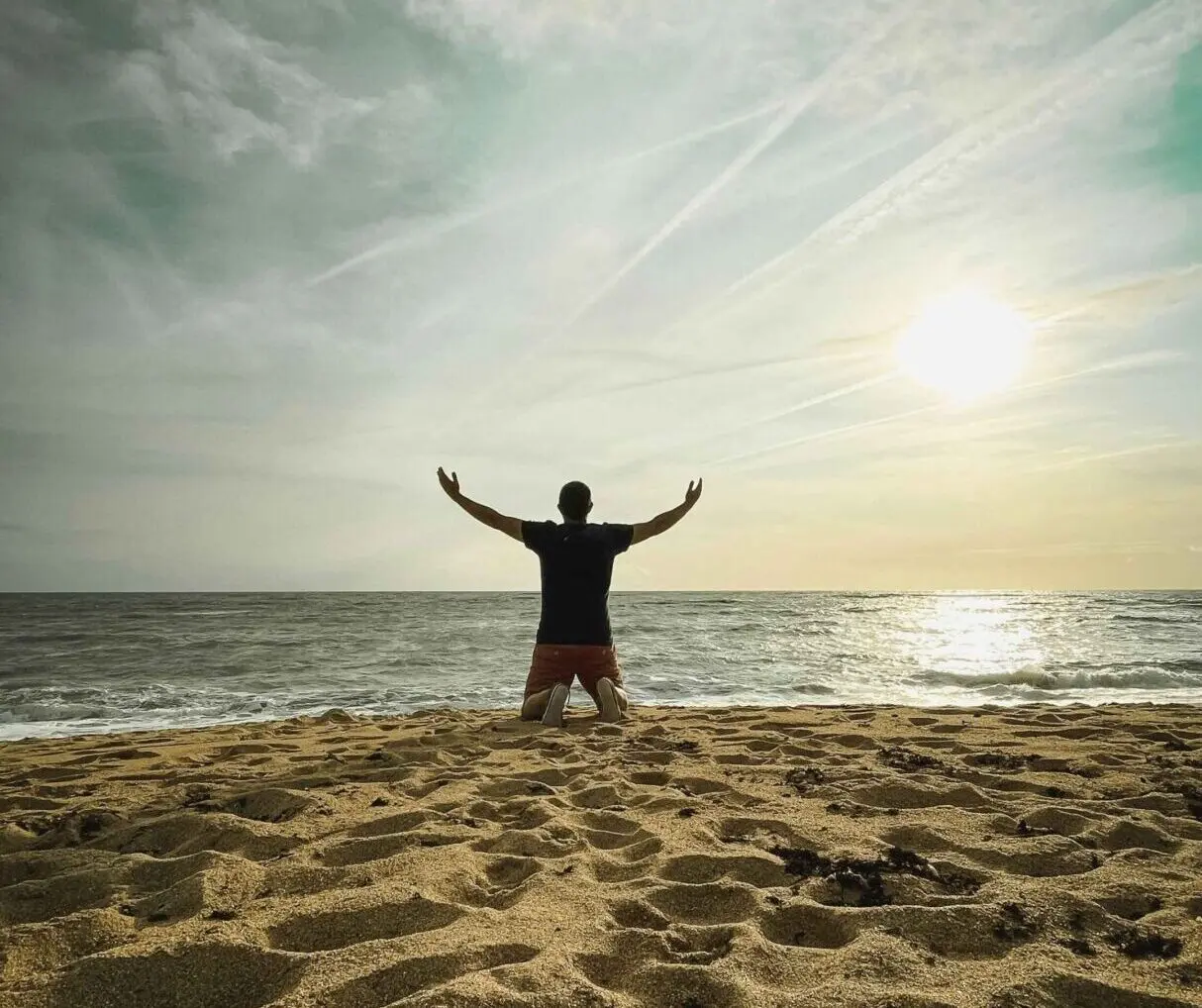 Person kneeling on beach facing the ocean.