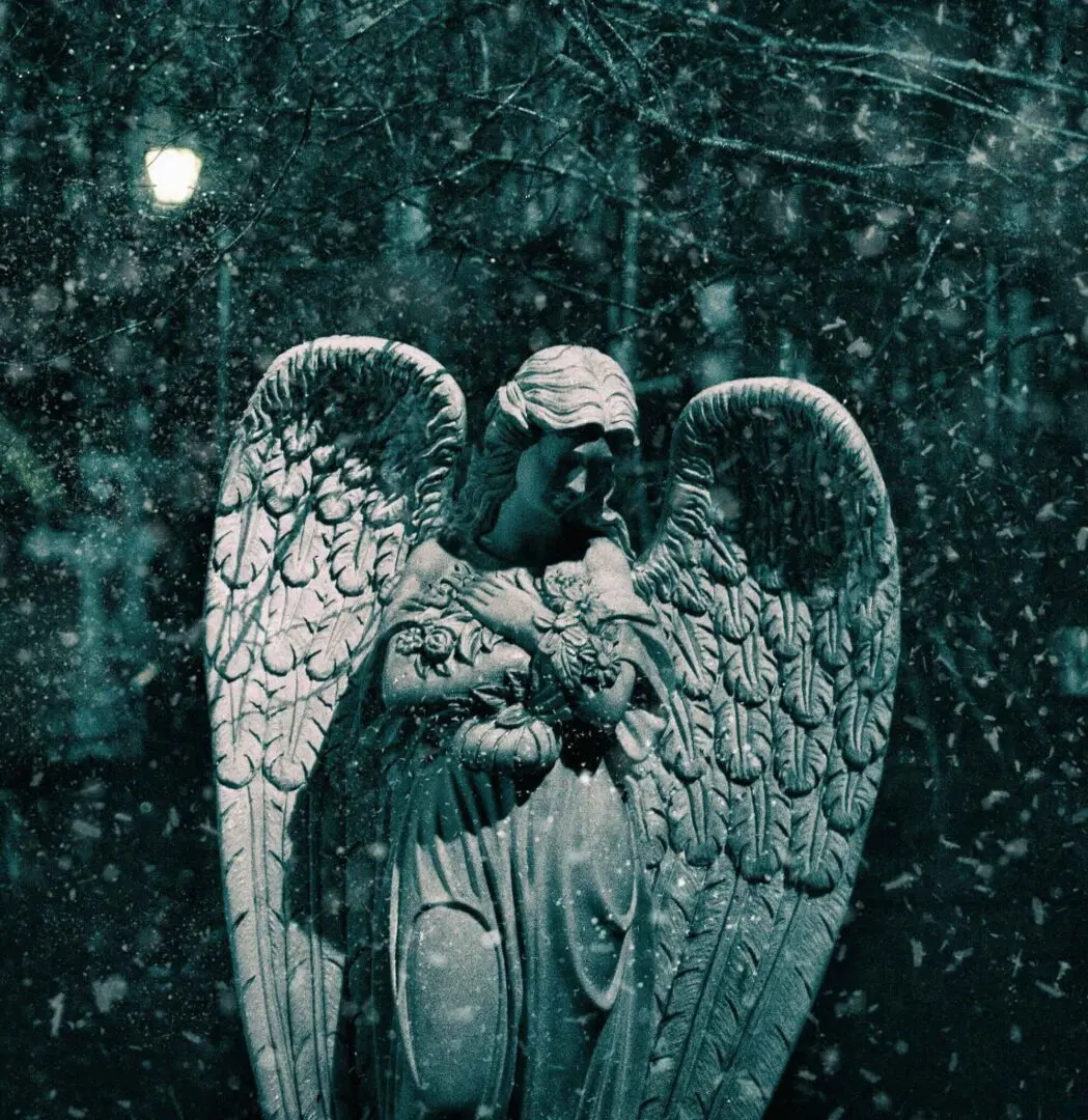 Angel statue in snow at night.