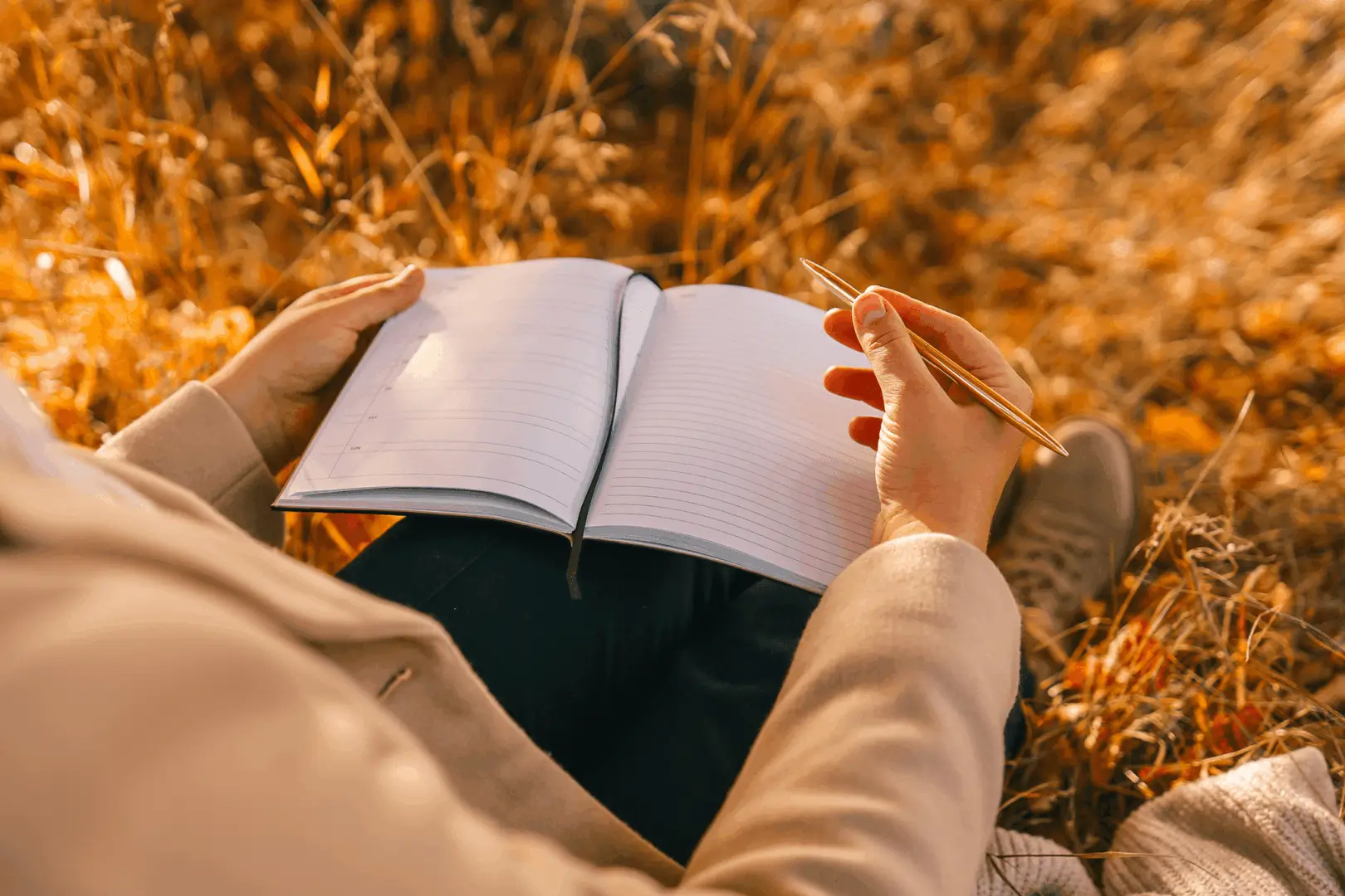 Person writing in notebook outdoors, autumn setting.