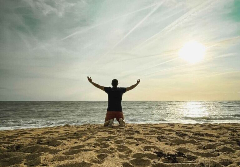 Person kneeling on beach facing the ocean.