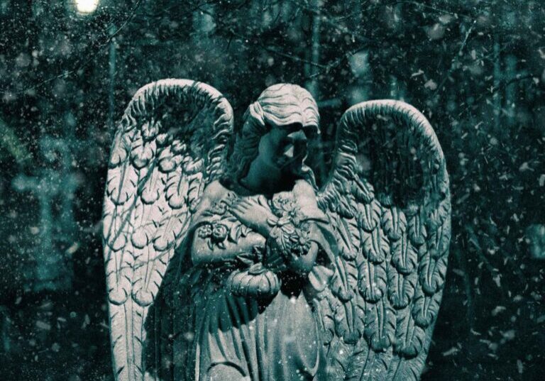 Angel statue in snow at night.
